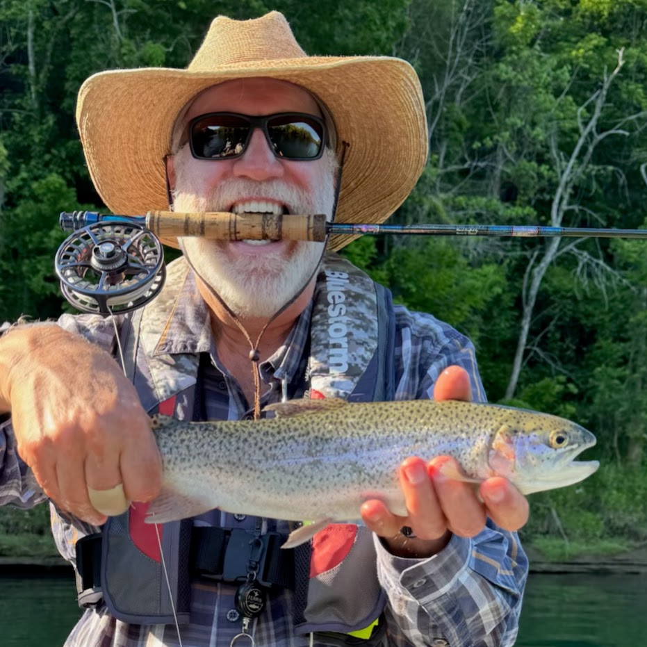 A smiling fly fisherman holding a bright rainbow trout next to a fly rod on the Cumberland River in Burkesville, Kentucky.