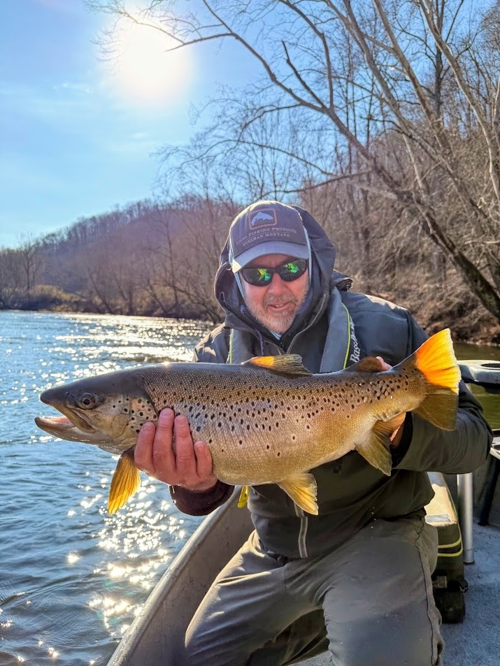 Captain Jeff Sharpe holding a large Brown Trout while fly fishing from a power boat.