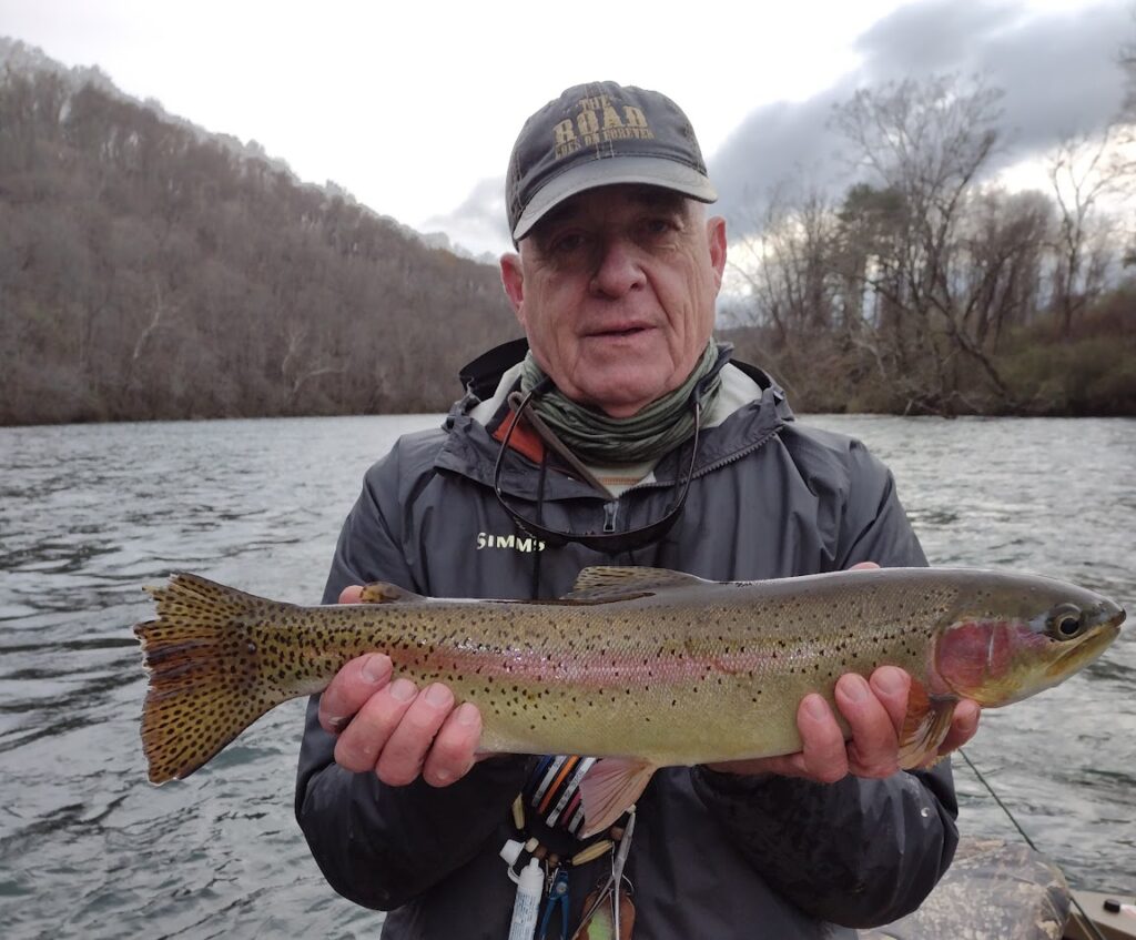 A fly fishing client bundled up in winter gear holding a massive trophy Rainbow Trout on a cold-weather guided boat trip on the Clinch River.