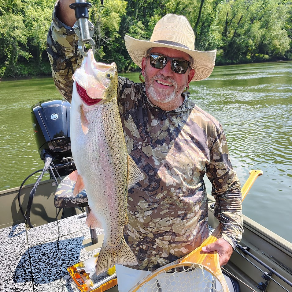 A happy fly fishing client wearing a cowboy hat and holding a massive giant Rainbow Trout on a guided boat trip on the Cumberland River.