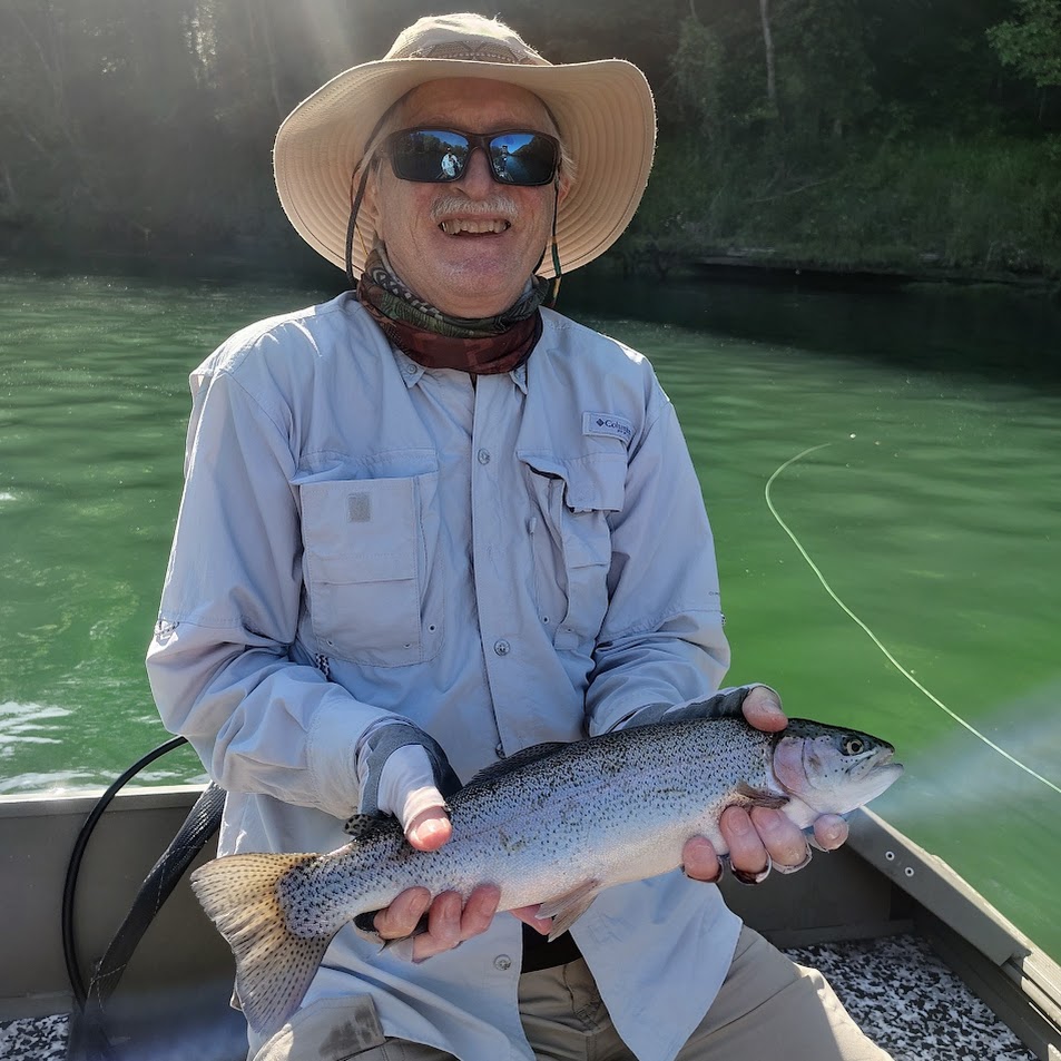 A smiling fly fisherman wearing sunglasses and a cap, holding up a healthy rainbow trout on a guided fly fishing trip on the Cumberland River.