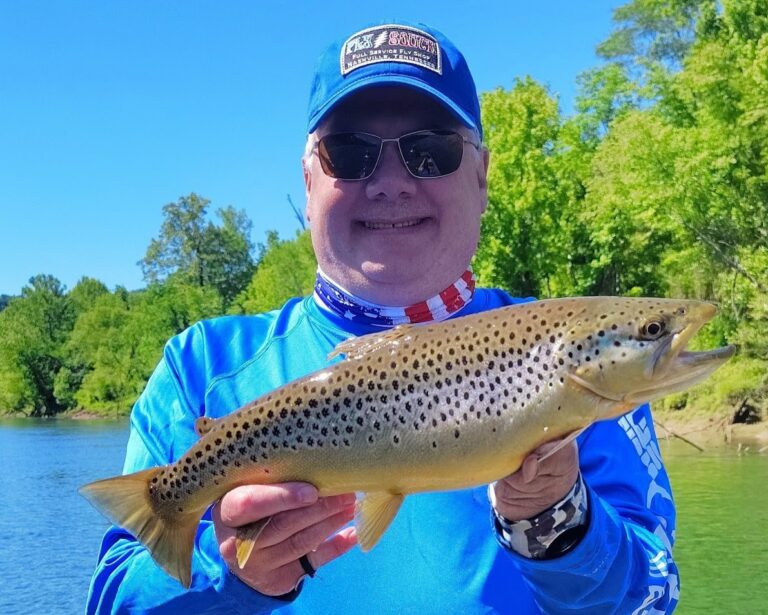 A happy angler holding a large, beautifully colored trophy brown trout caught while fly fishing on the Cumberland River.