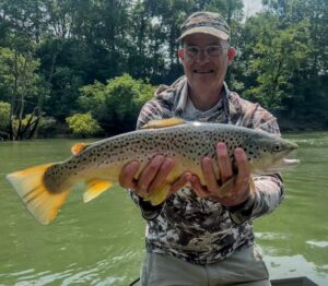 An angler in a camo cap proudly holding a heavy trophy Brown Trout caught while fly fishing on a guided boat trip on the Cumberland River.