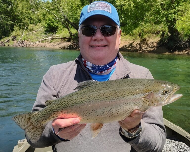 A happy angler holding a large, beautifully colored trophy rainbow trout caught while fly fishing on the Cumberland River.