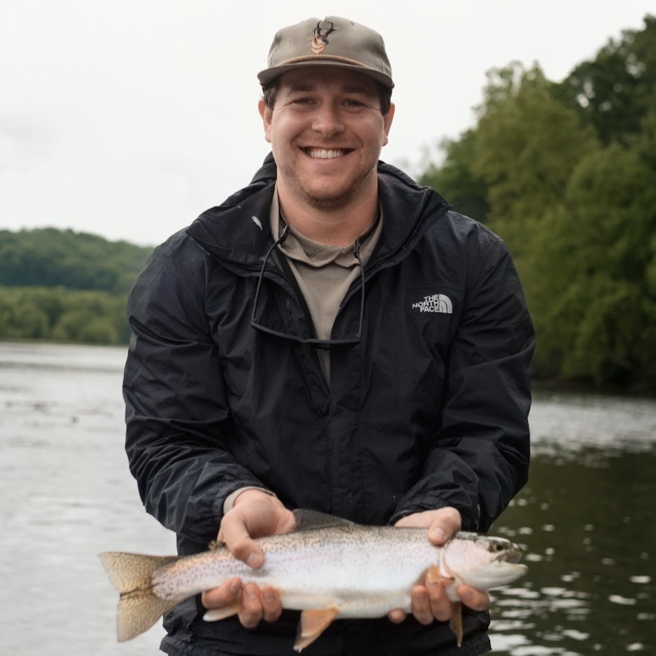 A smiling fly fisherman wearing a cap and jacket, holding a clean rainbow trout caught on a dry fly on the Holston River.