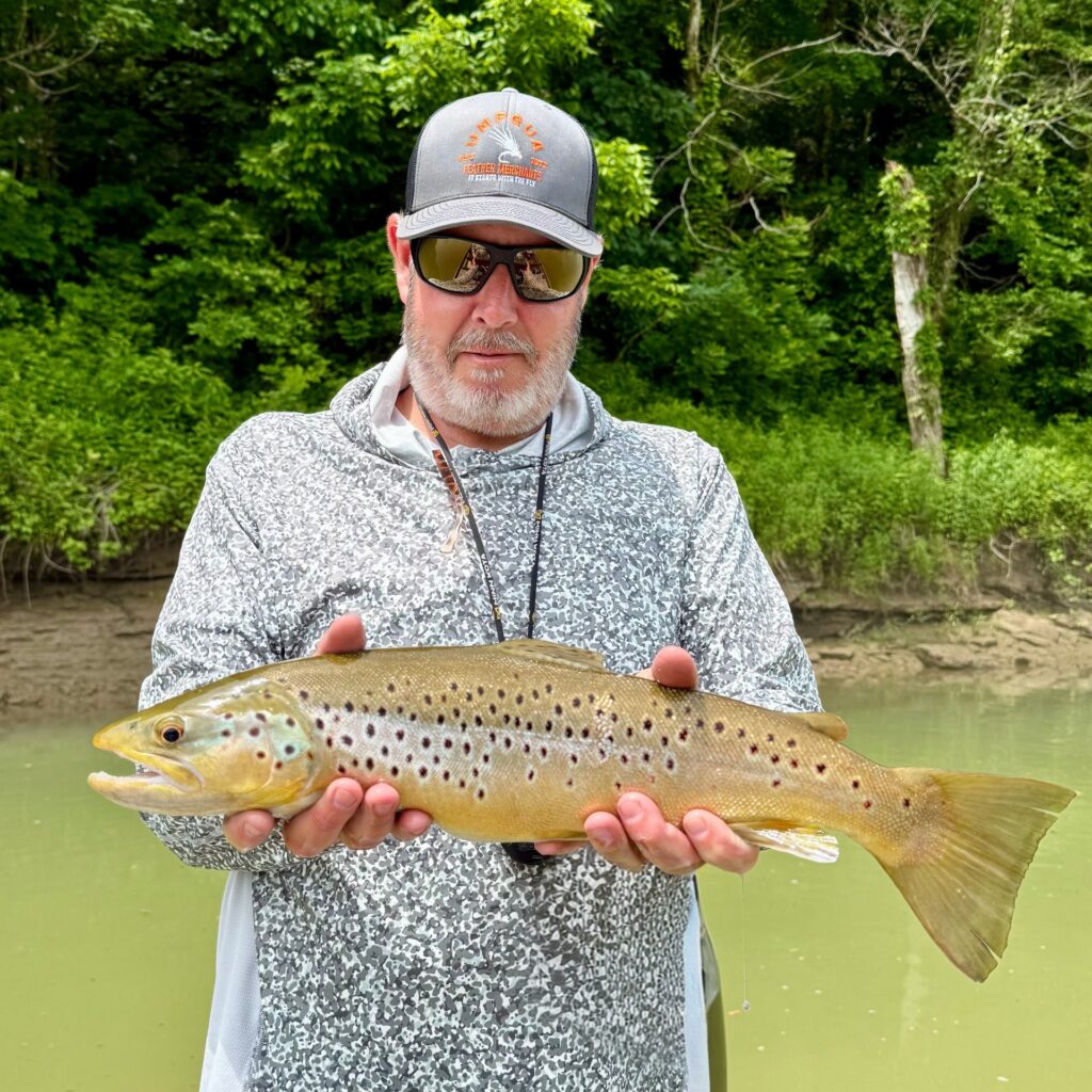 Captain Jeff Sharpe holding a massive 22-inch brown trout caught on a large black streamer in high, stained water on the Cumberland River.