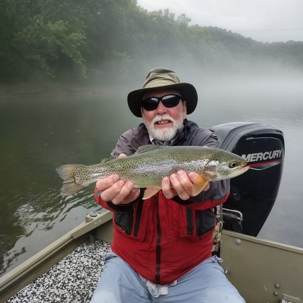 A happy angler holding a large, vibrant rainbow trout caught on a fly rod on the Cumberland River in Burkesville, Kentucky.