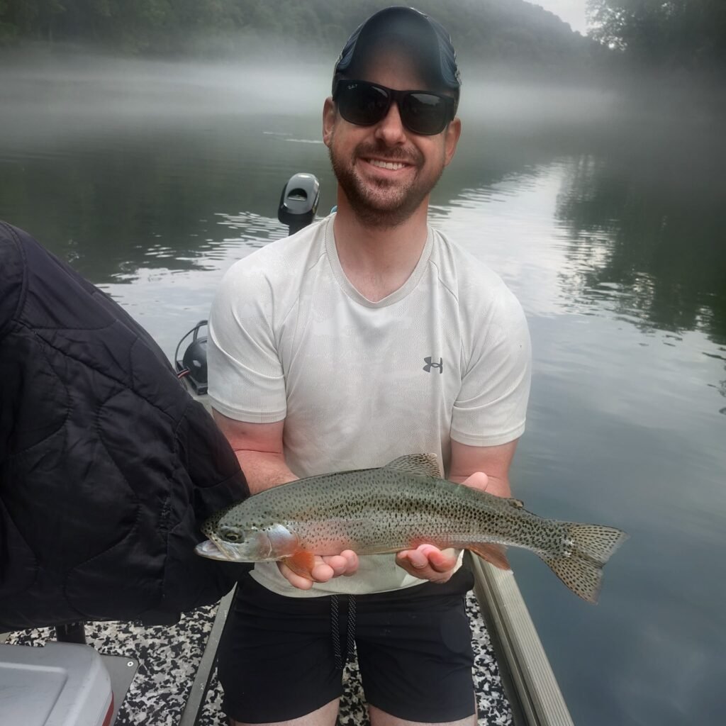 A man holding a vibrant rainbow trout caught on the Cumberland River in Burkesville, Kentucky.