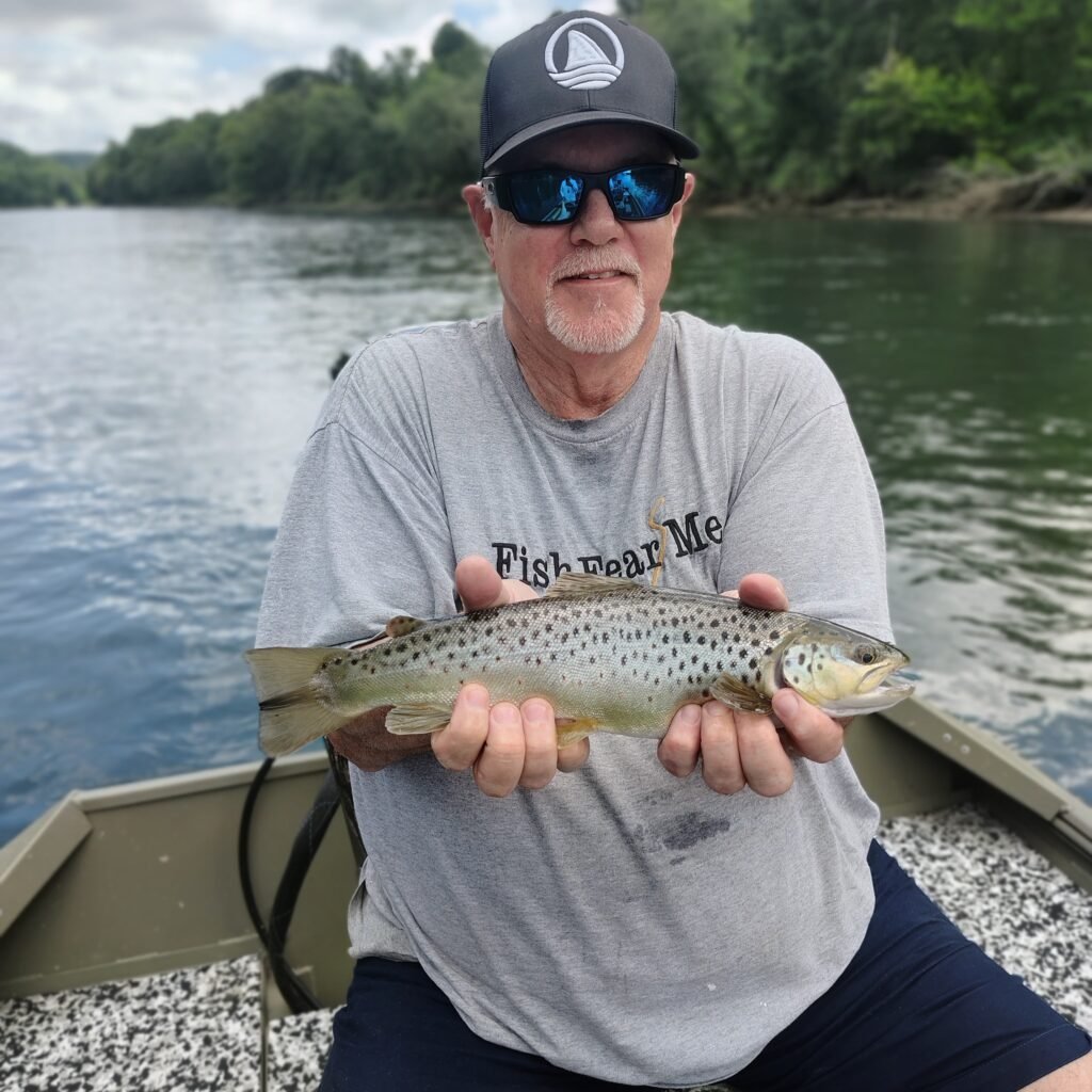 A man holding a healthy brown trout caught on a fly rod while standing in the Cumberland River near Burkesville, Kentucky.