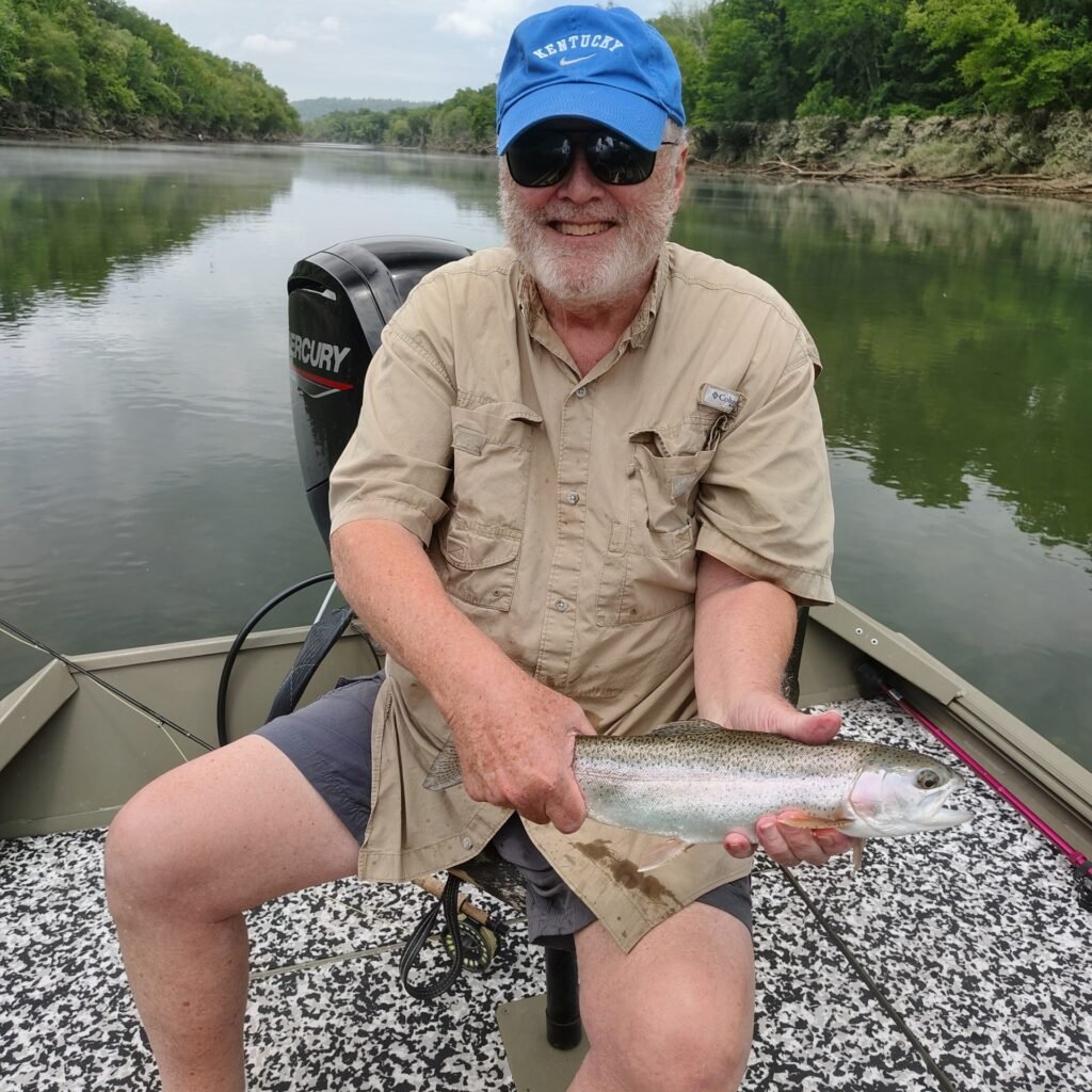 A man holding a vibrant rainbow trout caught on the Cumberland River in Burkesville, Kentucky.