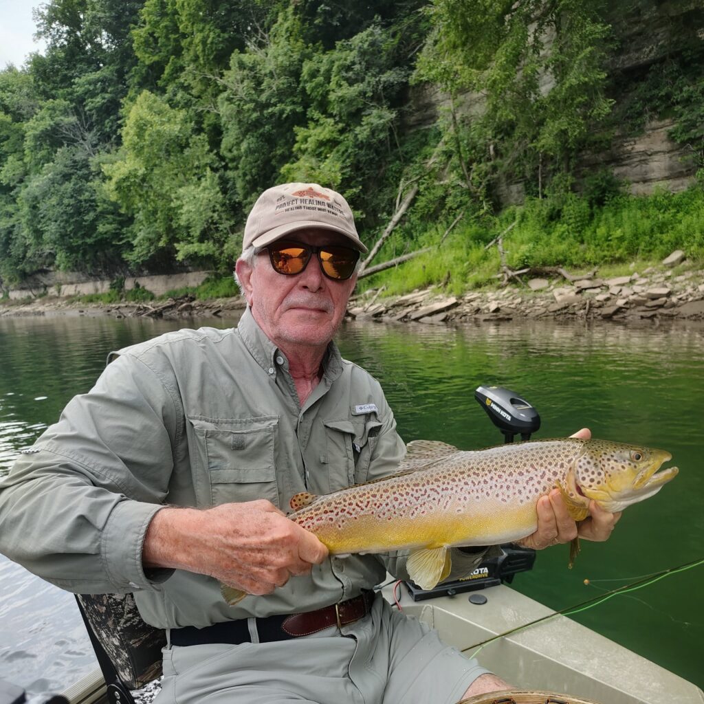 A happy angler holding a large, trophy-sized brown trout caught on a fly rod on the Cumberland River in Burkesville, Kentucky.