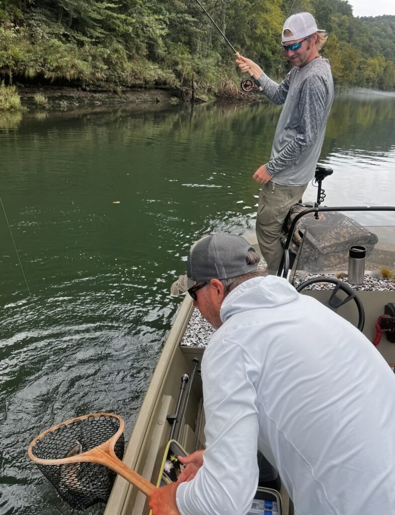 Guide netting a healthy rainbow trout next to a drift boat on the Cumberland River near Burkesville, Kentucky