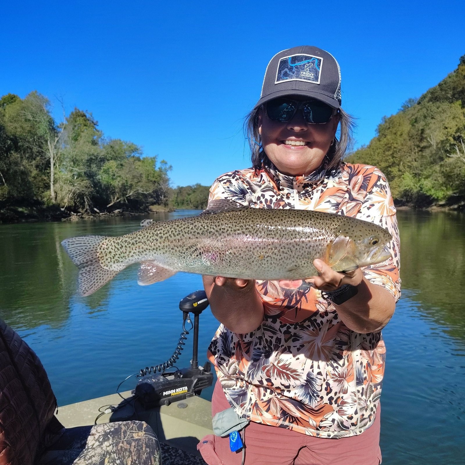 An angler holding a vibrant rainbow trout against a backdrop of autumn foliage on the Cumberland River in Burkesville, Kentucky.