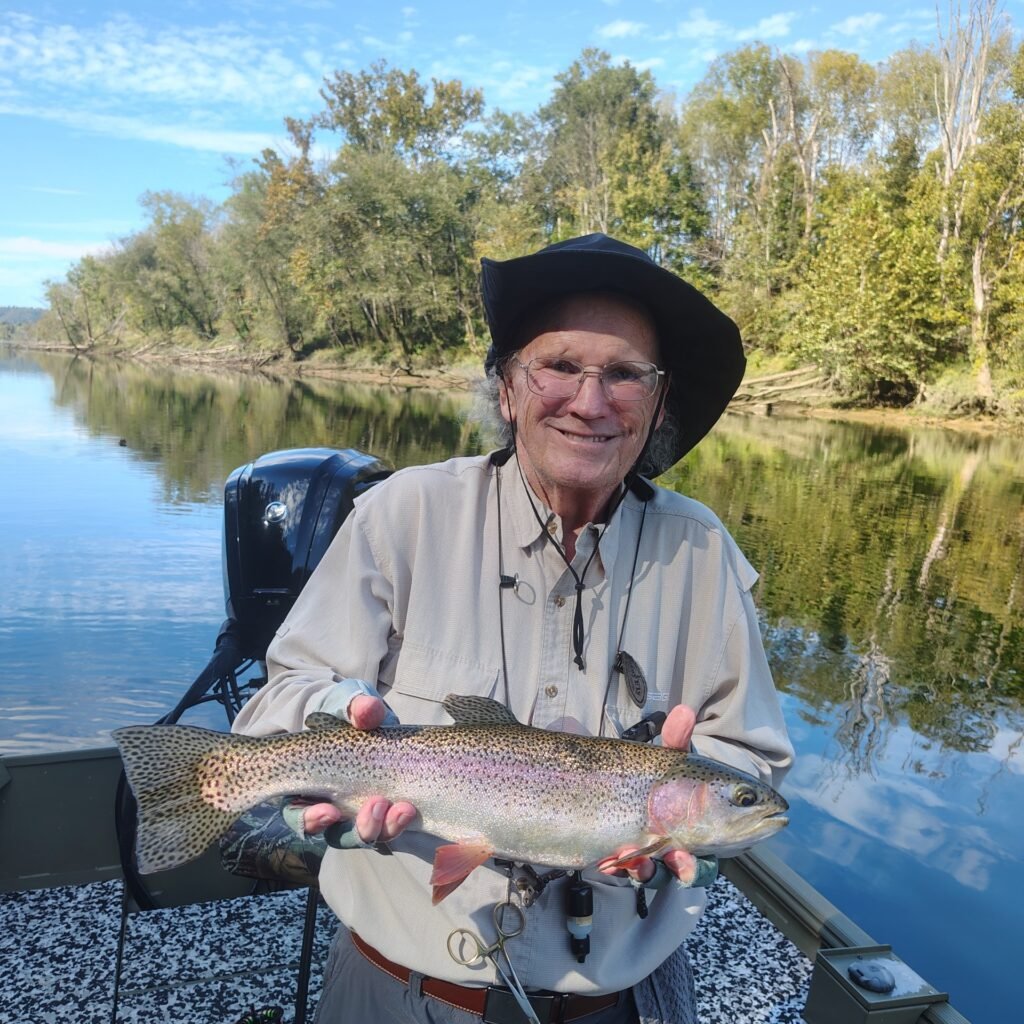 An angler holding a vibrant rainbow trout against a backdrop of autumn foliage on the Cumberland River in Burkesville, Kentucky.